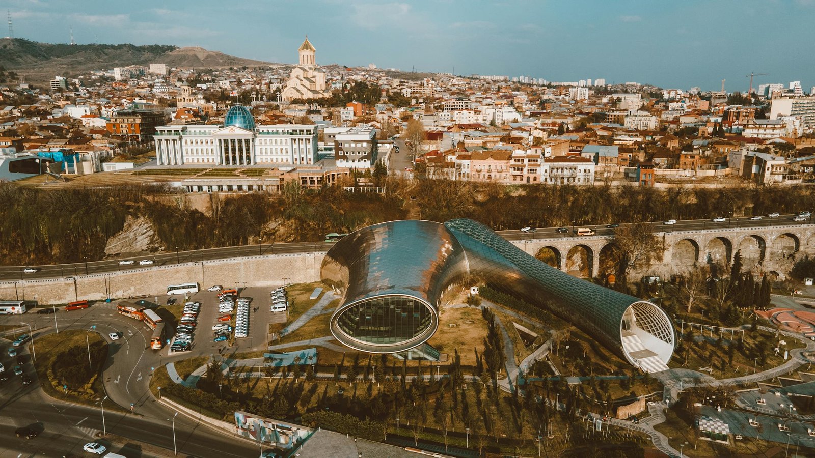 Discover the striking blend of modern architecture amidst Tbilisi's sprawling urban landscape from above.