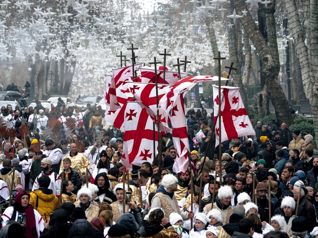 Festive crowd in a traditional Georgian parade displaying flags and cultural attire.